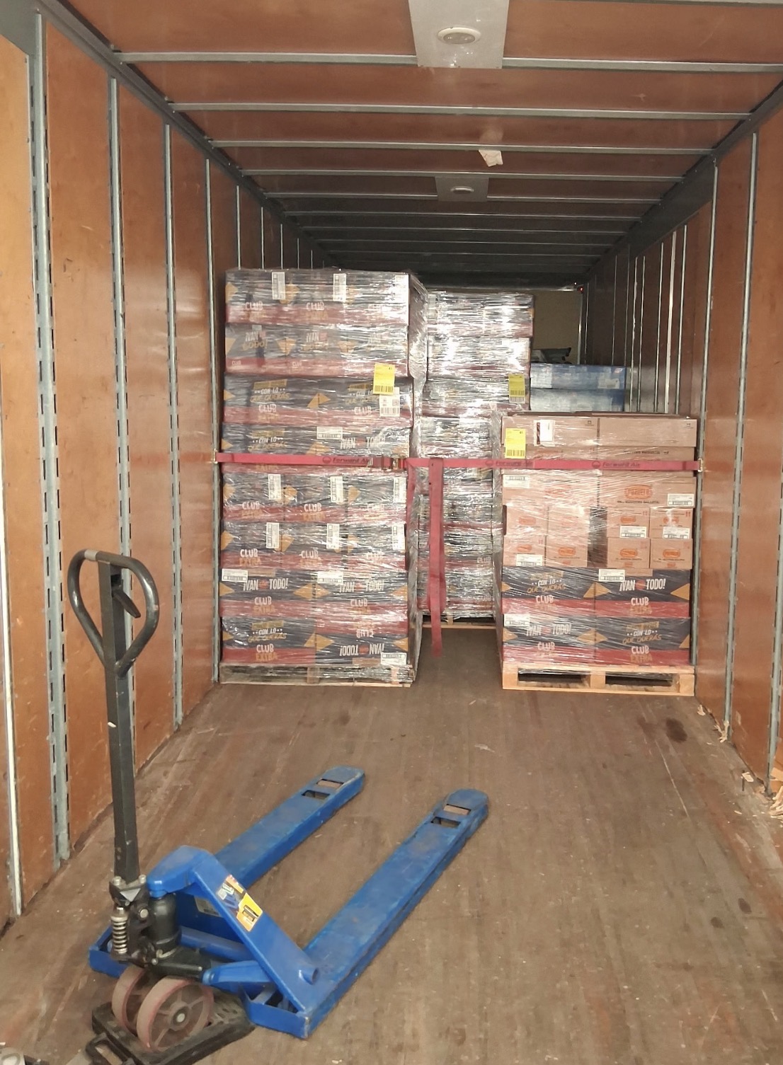 Shrink-wrapped pallets strapped inside a PrimePath trailer with a pallet jack at the door